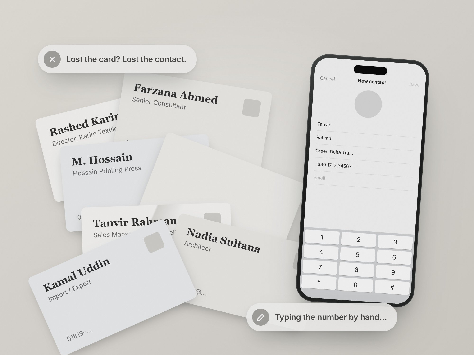 A messy pile of paper business cards next to a phone where someone is typing a contact's number by hand